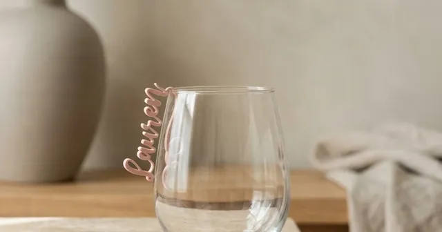 Pink script name tag clipped on the rim of a wine glass.