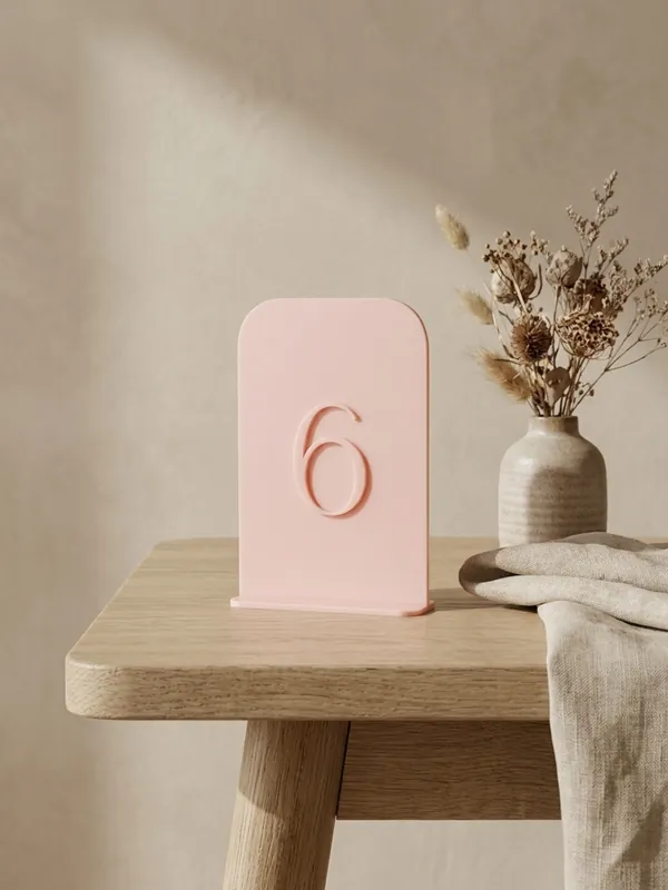 Pink card-shaped table number 6 on a wooden stool.